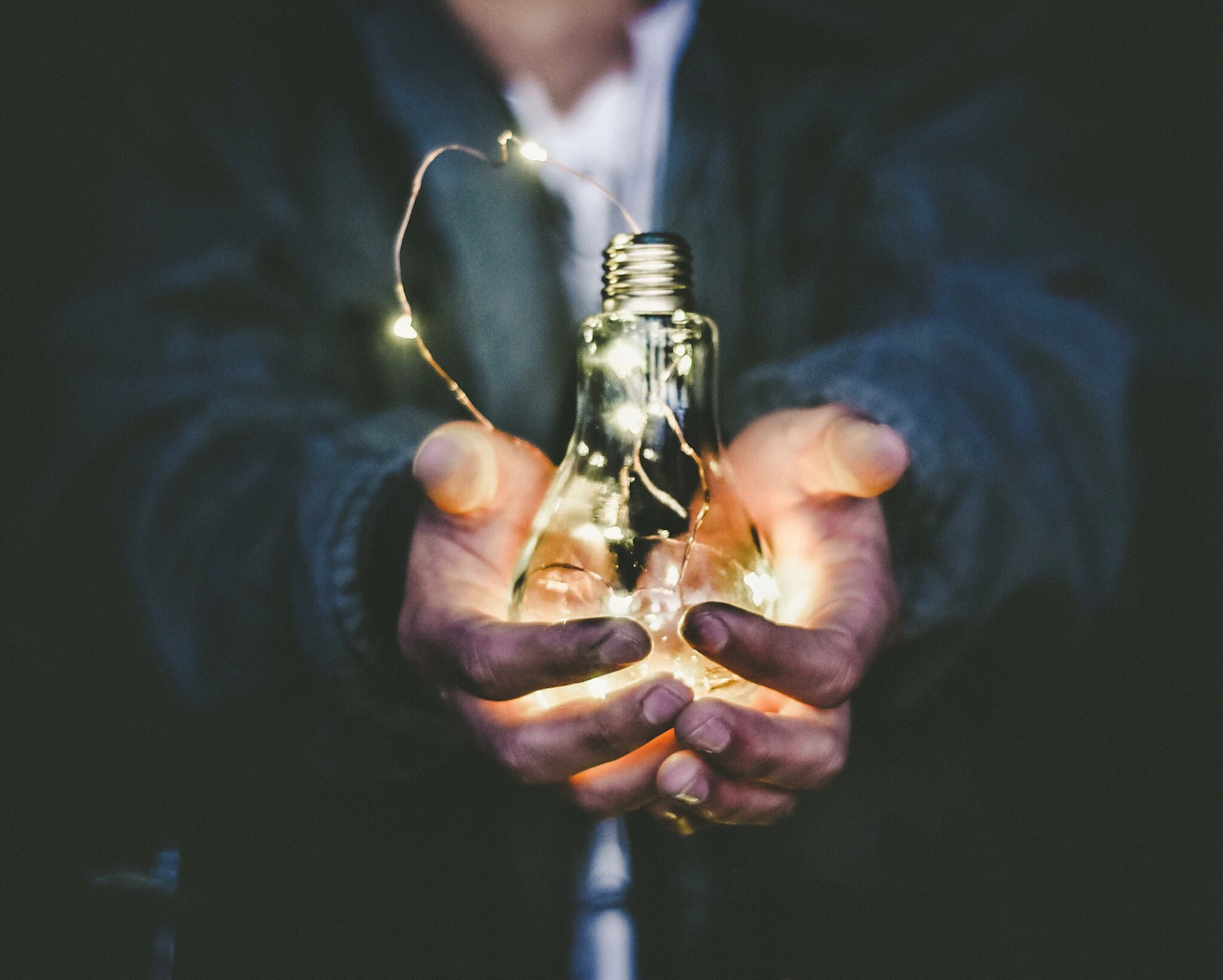 Two hands cupping a lit bulb wound with fine wire